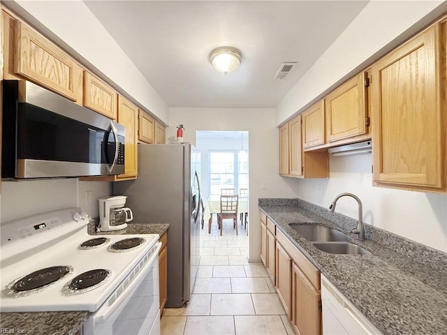 kitchen featuring light brown cabinets, white appliances, light tile patterned flooring, dark stone countertops, and sink