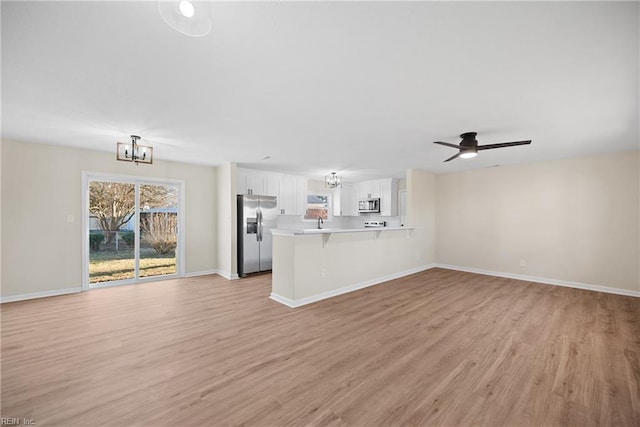 unfurnished living room featuring ceiling fan with notable chandelier and light wood-type flooring