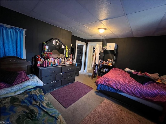 carpeted bedroom featuring a paneled ceiling and wooden walls