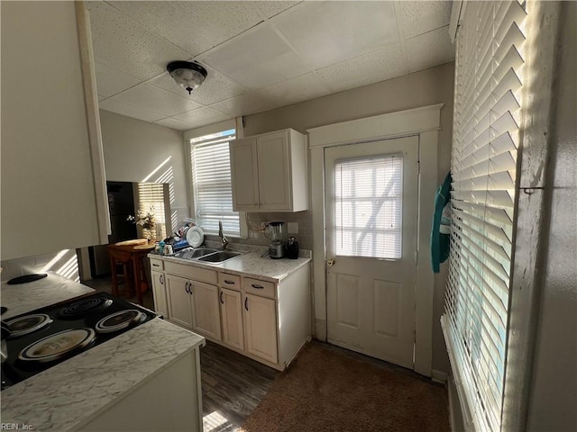 kitchen with a paneled ceiling, white cabinets, stovetop, and sink