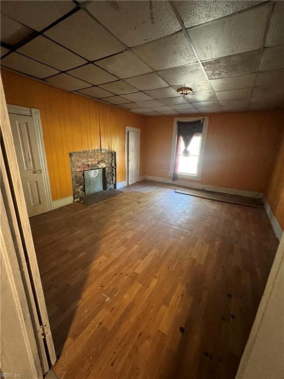 unfurnished living room with a paneled ceiling, hardwood / wood-style floors, and wooden walls