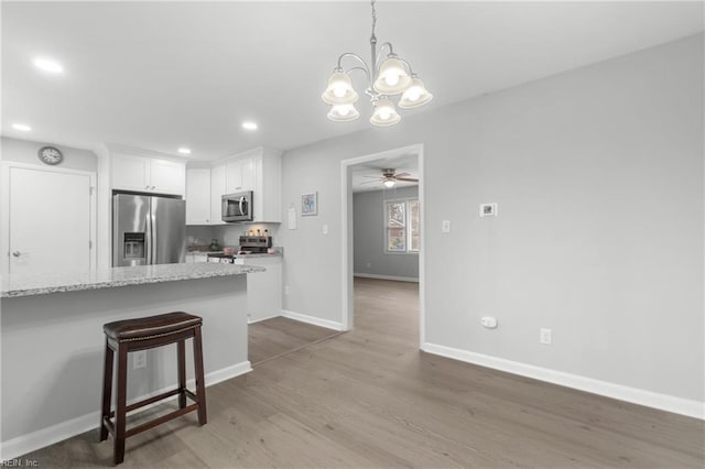 kitchen featuring white cabinetry, stainless steel appliances, decorative light fixtures, a kitchen breakfast bar, and ceiling fan with notable chandelier