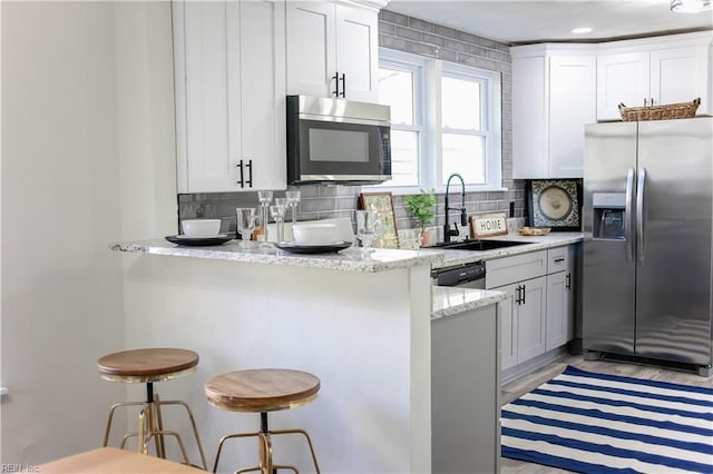 kitchen with sink, white cabinetry, light stone countertops, a kitchen breakfast bar, and stainless steel appliances