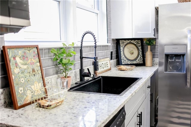 kitchen featuring decorative backsplash, sink, stainless steel fridge with ice dispenser, white cabinets, and light stone counters