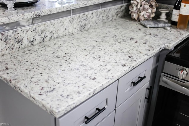 details featuring stainless steel range with electric stovetop, white cabinetry, and light stone countertops