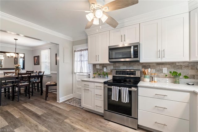 kitchen with stainless steel appliances, crown molding, ceiling fan with notable chandelier, and white cabinetry