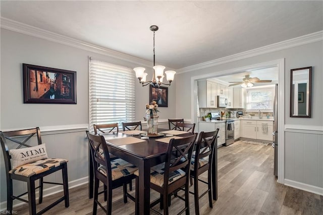 dining room with ceiling fan with notable chandelier, sink, light hardwood / wood-style flooring, and crown molding