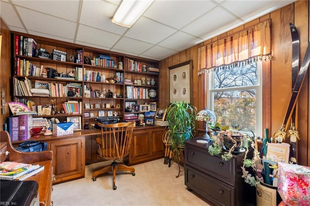 office space with a paneled ceiling, light colored carpet, and wood walls