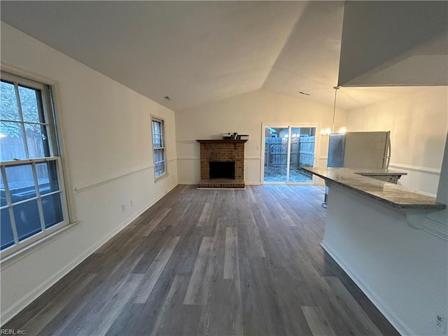 unfurnished living room featuring dark hardwood / wood-style flooring, lofted ceiling, a fireplace, and a chandelier