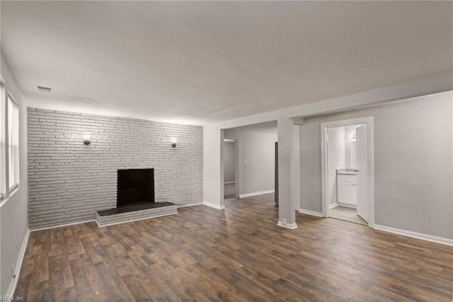 unfurnished living room with a fireplace, brick wall, and dark hardwood / wood-style flooring