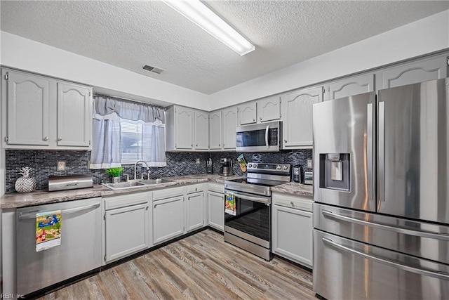 kitchen with a textured ceiling, stainless steel appliances, light hardwood / wood-style floors, sink, and decorative backsplash