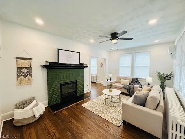 living room featuring radiator heating unit, a wall unit AC, ceiling fan, dark hardwood / wood-style flooring, and a fireplace