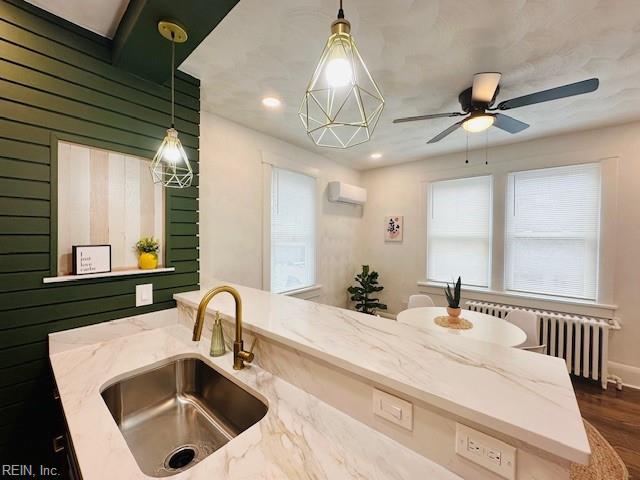 kitchen with sink, hanging light fixtures, light stone countertops, and an AC wall unit