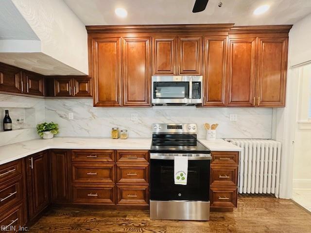 kitchen featuring dark wood-type flooring, radiator heating unit, appliances with stainless steel finishes, and tasteful backsplash