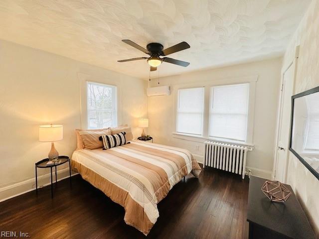 bedroom with ceiling fan, a wall mounted AC, radiator, and dark wood-type flooring