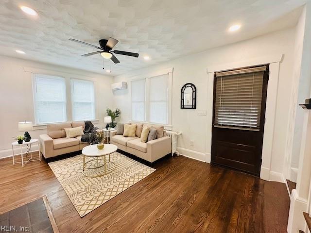 living room with an AC wall unit, ceiling fan, and dark hardwood / wood-style flooring