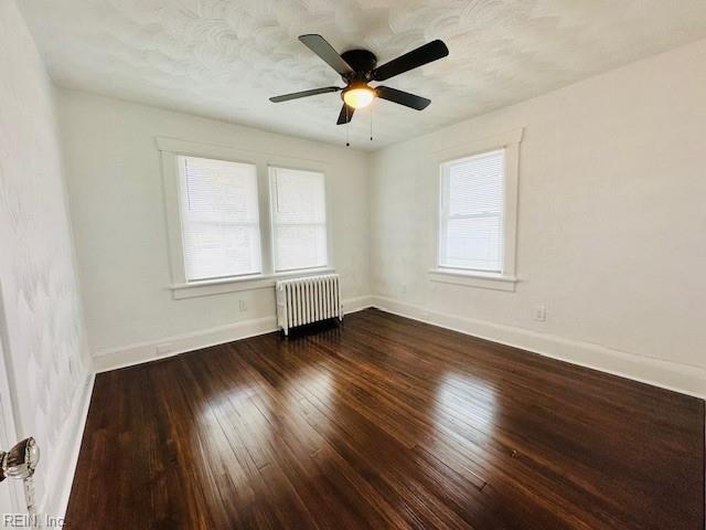 empty room with ceiling fan, dark wood-type flooring, and radiator