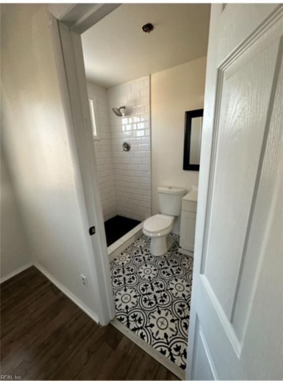 bathroom with wood-type flooring, toilet, and a tile shower