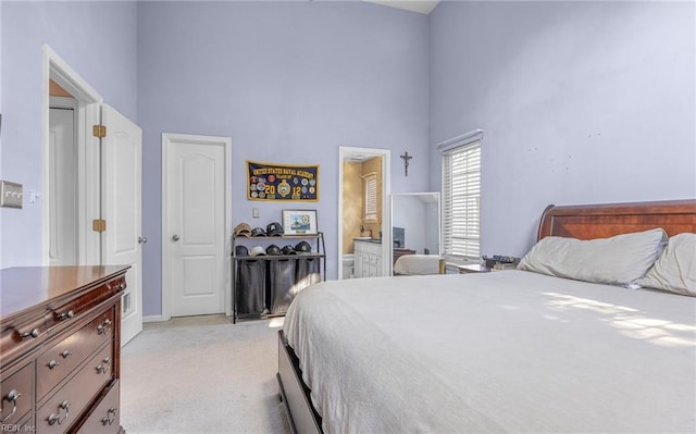 carpeted bedroom with ensuite bathroom and a towering ceiling