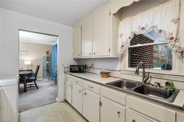 kitchen with sink, white cabinetry, washer / dryer, and light carpet