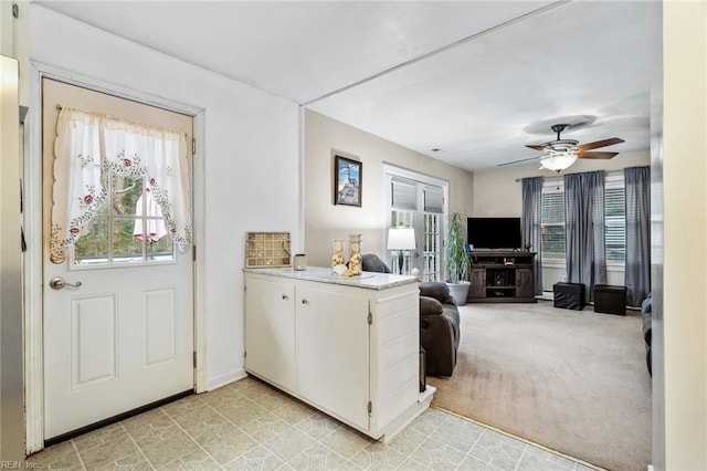 kitchen featuring white cabinets, a fireplace, kitchen peninsula, ceiling fan, and light colored carpet