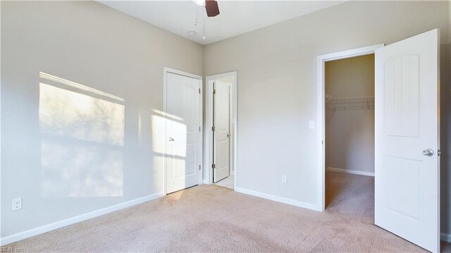 unfurnished bedroom featuring ceiling fan, a walk in closet, light carpet, and a closet