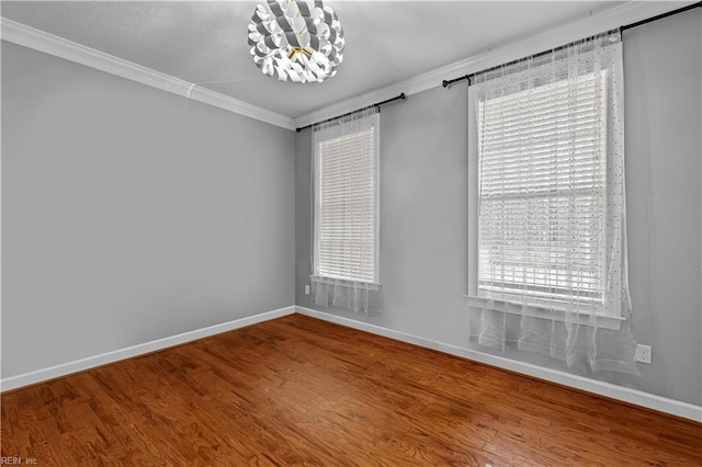 spare room with wood-type flooring, ornamental molding, a wealth of natural light, and a notable chandelier