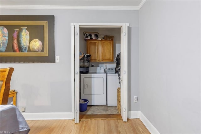 washroom with cabinets, light wood-type flooring, crown molding, and washing machine and clothes dryer