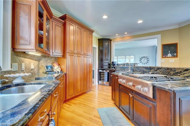 kitchen featuring light hardwood / wood-style flooring, ornamental molding, stainless steel gas cooktop, beverage cooler, and dark stone counters