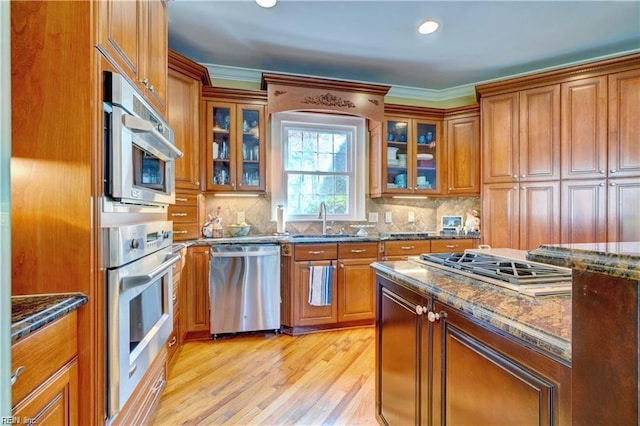 kitchen featuring sink, light hardwood / wood-style flooring, appliances with stainless steel finishes, backsplash, and dark stone counters