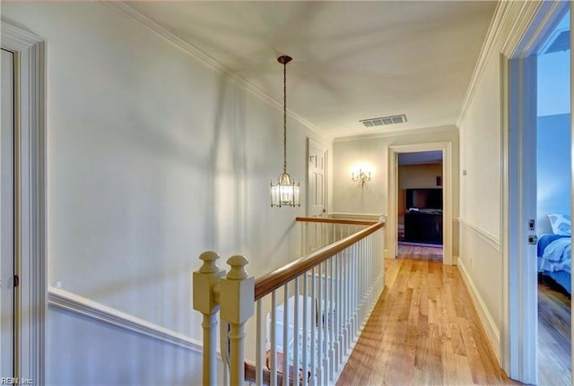 corridor with crown molding, a chandelier, and light hardwood / wood-style floors