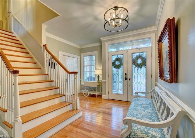 foyer with french doors, ornamental molding, an inviting chandelier, and light hardwood / wood-style floors