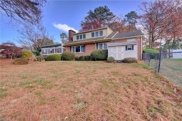 view of front of house featuring a front lawn, a sunroom, and a storage unit