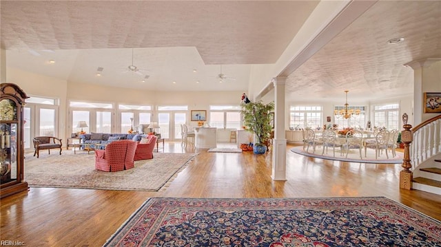 unfurnished living room featuring ceiling fan with notable chandelier, wood-type flooring, and decorative columns