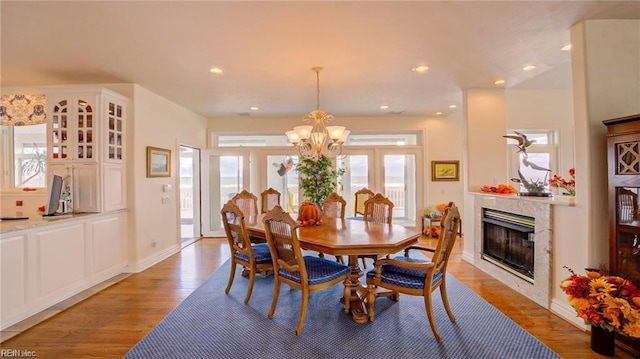 dining room with light wood-type flooring, a high end fireplace, and a notable chandelier