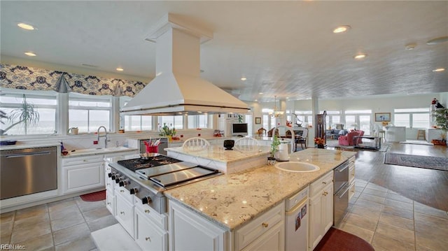 kitchen with light stone countertops, appliances with stainless steel finishes, a kitchen island, island exhaust hood, and sink