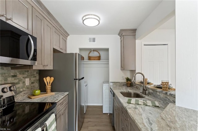 kitchen with sink, light stone counters, tasteful backsplash, light hardwood / wood-style flooring, and stainless steel appliances