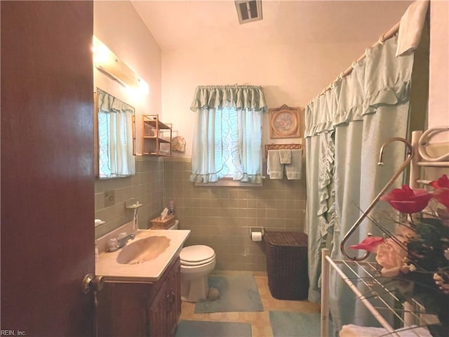 bathroom with toilet, vanity, and tile walls