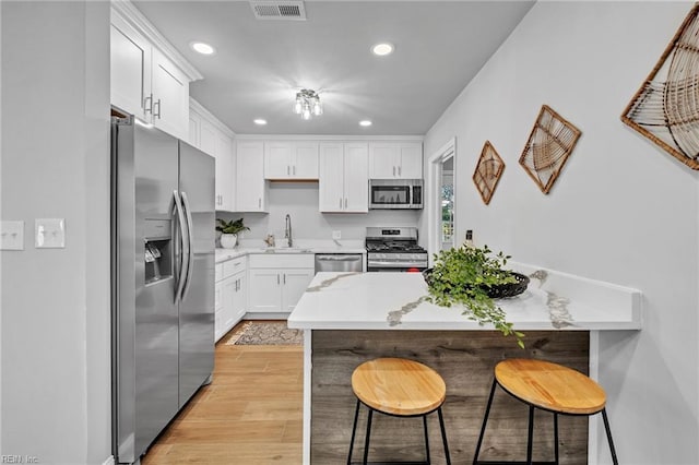 kitchen with white cabinetry, stainless steel appliances, sink, a breakfast bar, and light hardwood / wood-style flooring