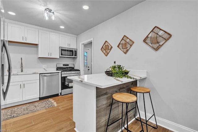 kitchen with a breakfast bar, sink, light hardwood / wood-style flooring, appliances with stainless steel finishes, and white cabinets