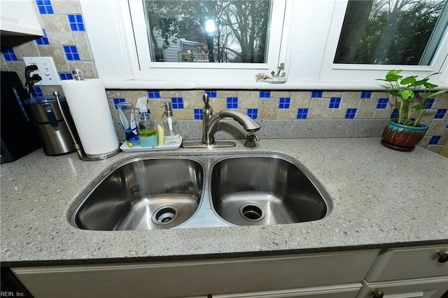 interior details featuring decorative backsplash, white cabinets, and sink