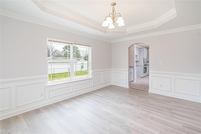 unfurnished room with light wood-type flooring, ornamental molding, a raised ceiling, and a notable chandelier