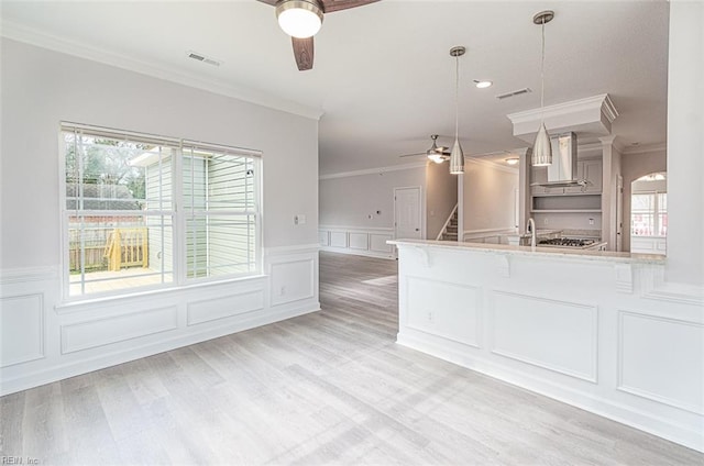 kitchen featuring decorative light fixtures, wall chimney exhaust hood, a wealth of natural light, and ornamental molding