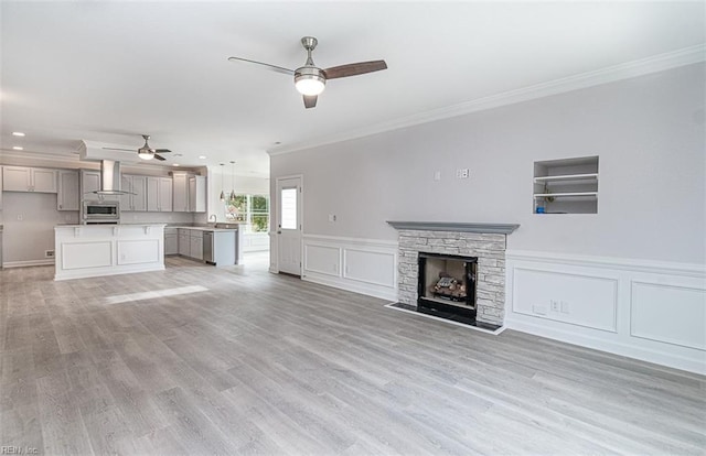 unfurnished living room featuring ceiling fan, light hardwood / wood-style floors, a stone fireplace, ornamental molding, and built in shelves