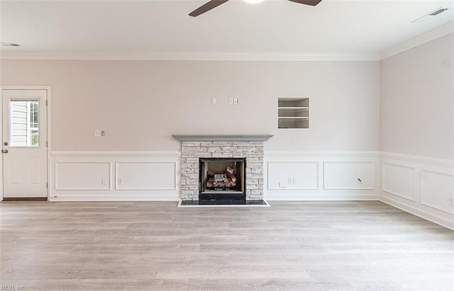 unfurnished living room with ceiling fan, a stone fireplace, ornamental molding, and light hardwood / wood-style flooring