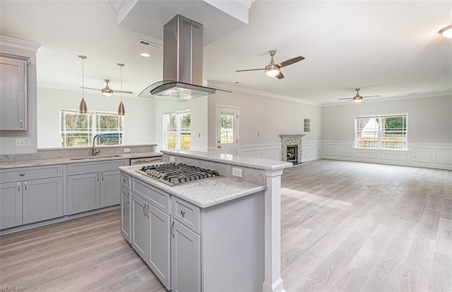 kitchen with island exhaust hood, sink, hanging light fixtures, light wood-type flooring, and stainless steel gas stovetop