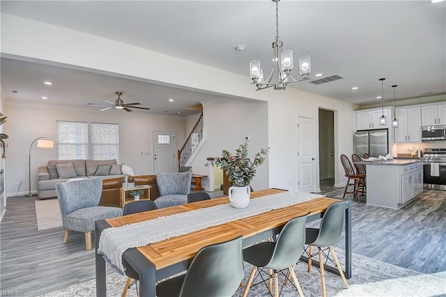 dining area with ceiling fan with notable chandelier, ornamental molding, and light hardwood / wood-style floors