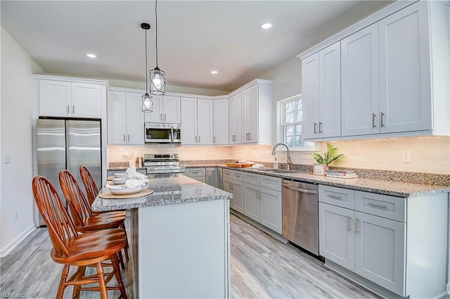 kitchen with decorative light fixtures, light hardwood / wood-style floors, a kitchen island, sink, and stainless steel appliances