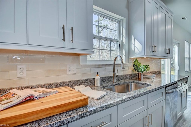 kitchen featuring light stone countertops, decorative backsplash, dishwasher, and sink