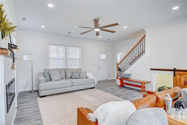 living room with ceiling fan, crown molding, a barn door, and wood-type flooring